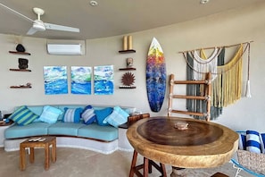 A living room with a curved sofa, a round wooden table, and a surfboard decoration.