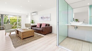 A modern living room with a sofa, chairs, a coffee table, and a glass shower enclosure. - The Oceana (Cape Town)