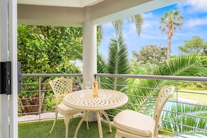 A covered outdoor area with a round table and chairs, a bottle of wine, and a view of a pool and palm trees. - The Oceana (Cape Town)