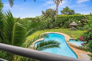 A swimming pool with a curved edge, surrounded by lush greenery and a thatched-roof gazebo. - The Oceana (Cape Town)