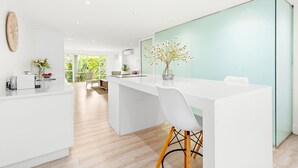 A modern kitchen with white cabinetry, a large island, and a glass partition. - The Oceana (Cape Town)