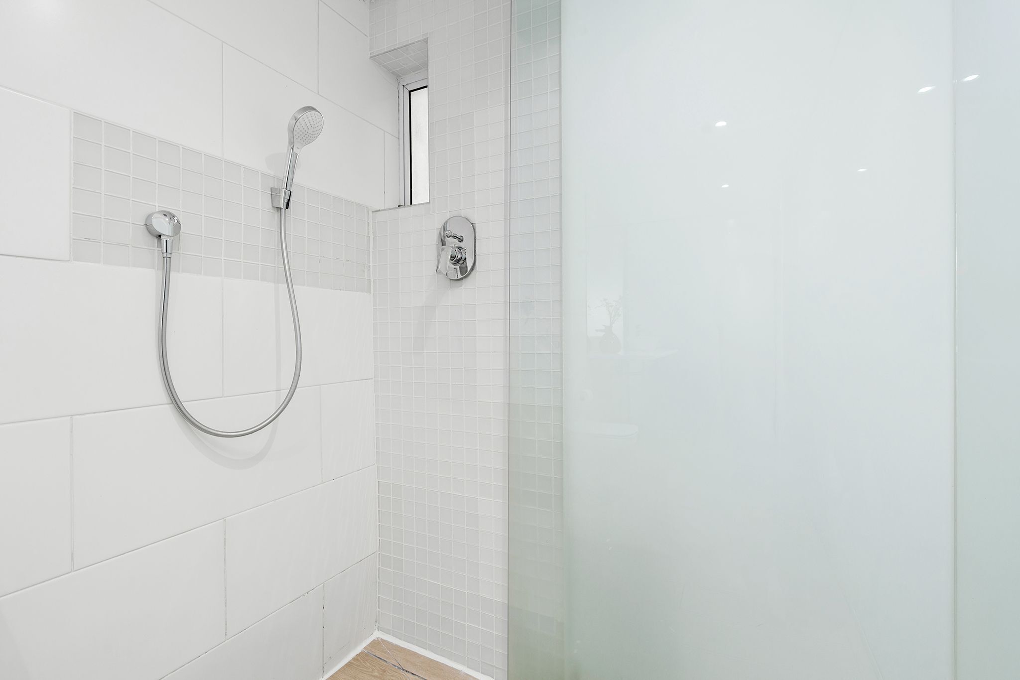 A modern bathroom with white tiled walls, a glass shower enclosure, and chrome fixtures.