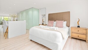 A modern bedroom with a large bed, bedside tables, a desk, and a view of the outdoors. - The Oceana (Cape Town)