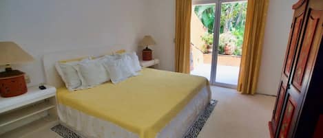 A bedroom with a bed, a nightstand, a lamp, a wardrobe, and a sliding glass door leading to a balcony.