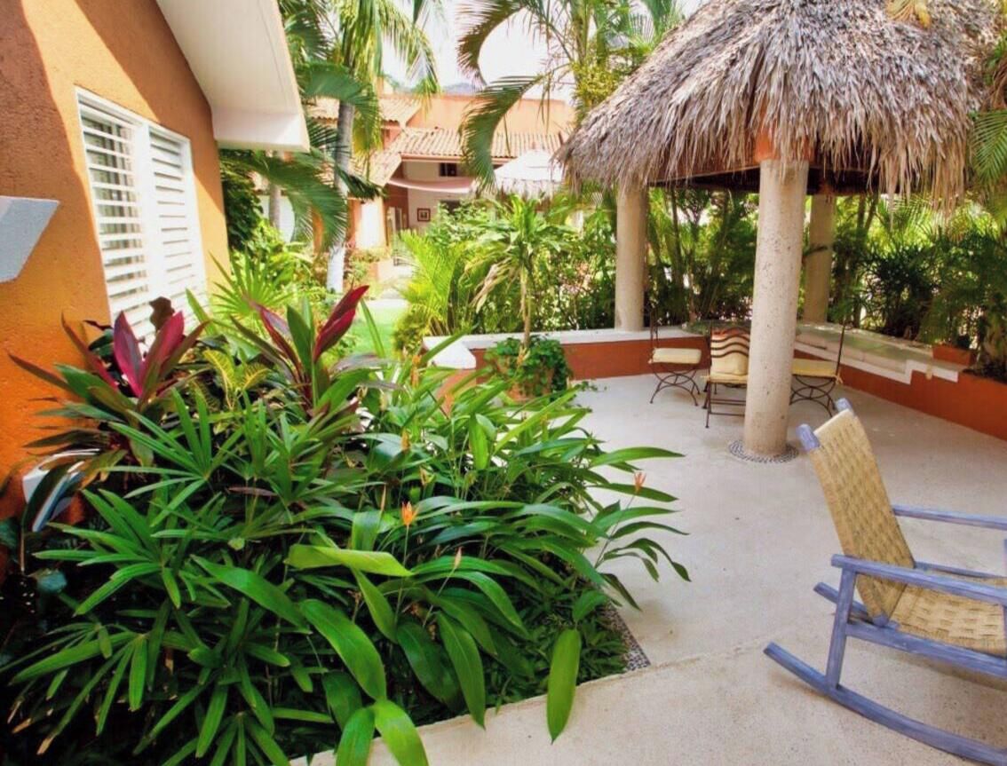A patio area with a thatched roof, outdoor furniture, and lush greenery.