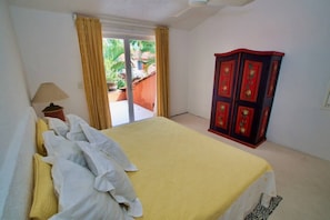 A bedroom with a bed, a wardrobe, a lamp, and a sliding glass door leading to an outdoor area. - Paracana 4 Bedroom Golf Course Villa (Ixtapa)