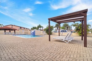 Une piscine sur le toit, agrémentée de chaises longues, d’une pergola et de palmiers en arrière-plan.