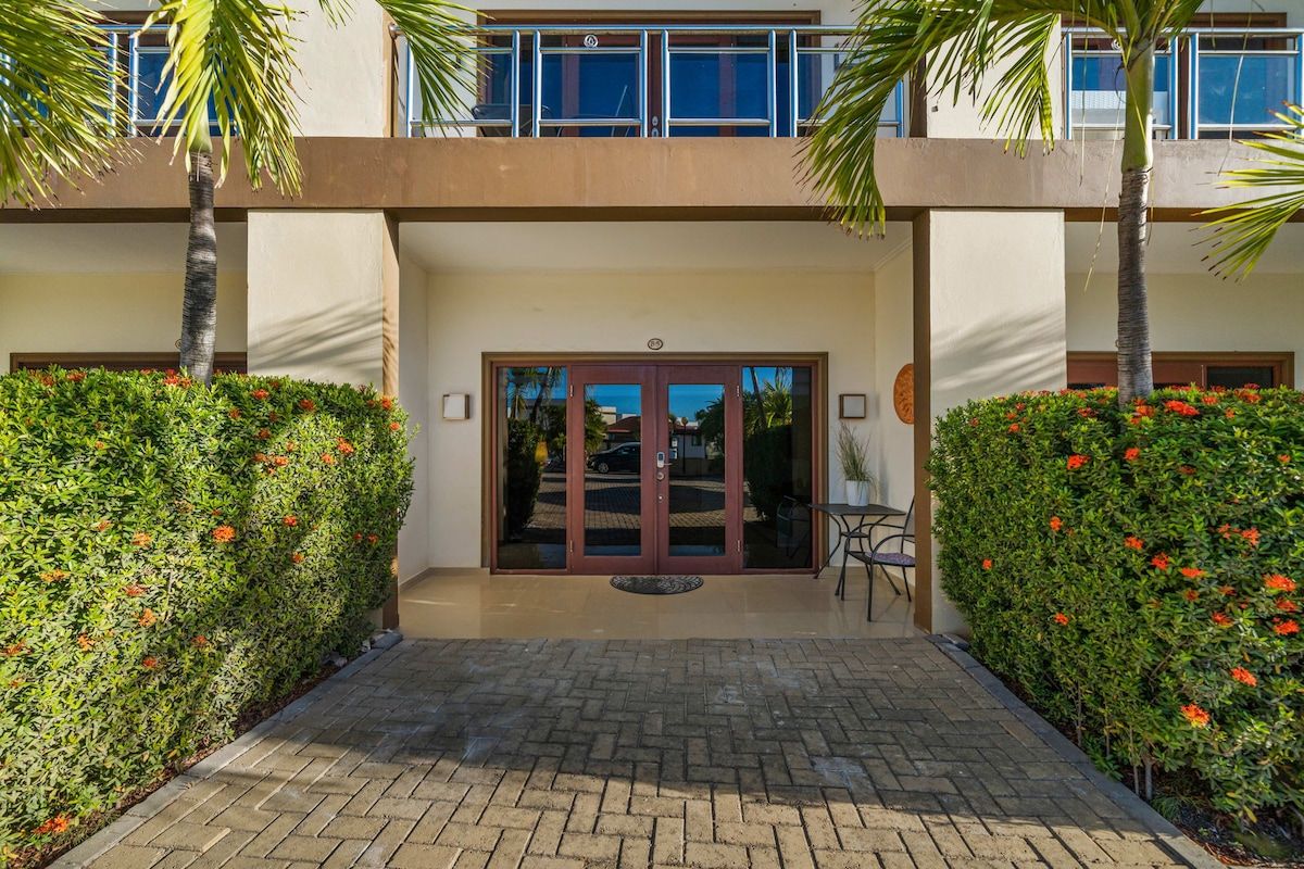 L’entrée d’un hôtel, avec une double porte, un chemin pavé et un petit espace extérieur aménagé avec des sièges.