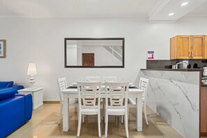 Une cuisine moderne avec des meubles blancs, un plan de travail en marbre et un coin repas comprenant des chaises et une table, le tout dans des tons blancs.