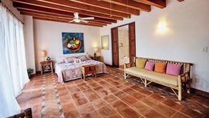 Ein Schlafzimmer mit einem Bett, einem Sofa, einem Deckenventilator, einem Gemälde und einem Fliesenboden.