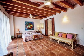 Ein Schlafzimmer mit einem Bett, einem Sofa, einem Deckenventilator, einem Gemälde und einem Fliesenboden.
