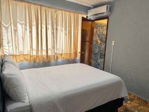 Ein Hotelzimmer mit Bett, Vorhängen, einer Klimaanlage und einer Steinwand.