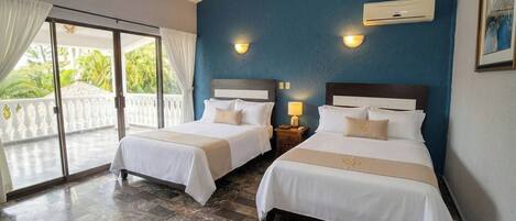 A hotel room with two beds, a ceiling fan, a sliding glass door to a balcony, and a wall-mounted air conditioning unit.