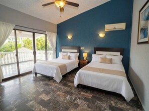 A hotel room with two beds, a ceiling fan, a sliding glass door to a balcony, and a wall-mounted air conditioning unit. - La Quinta de Don Hugo (Ixtapa)