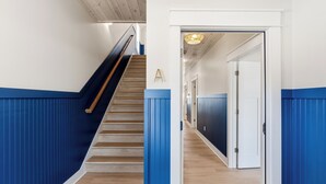 Un pasillo con escalera de madera, paneles azules y una puerta con marco blanco.