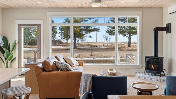 Una sala de estar acogedora con un sofá, una mesa, una silla, una chimenea y un ventanal con vistas a árboles y colinas.