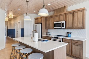 A modern kitchen with wooden cabinets, a central island, bar stools, and pendant lighting.
