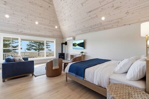 A bedroom with a bed, a sofa, a desk, and a large window with a view of trees and a lake.