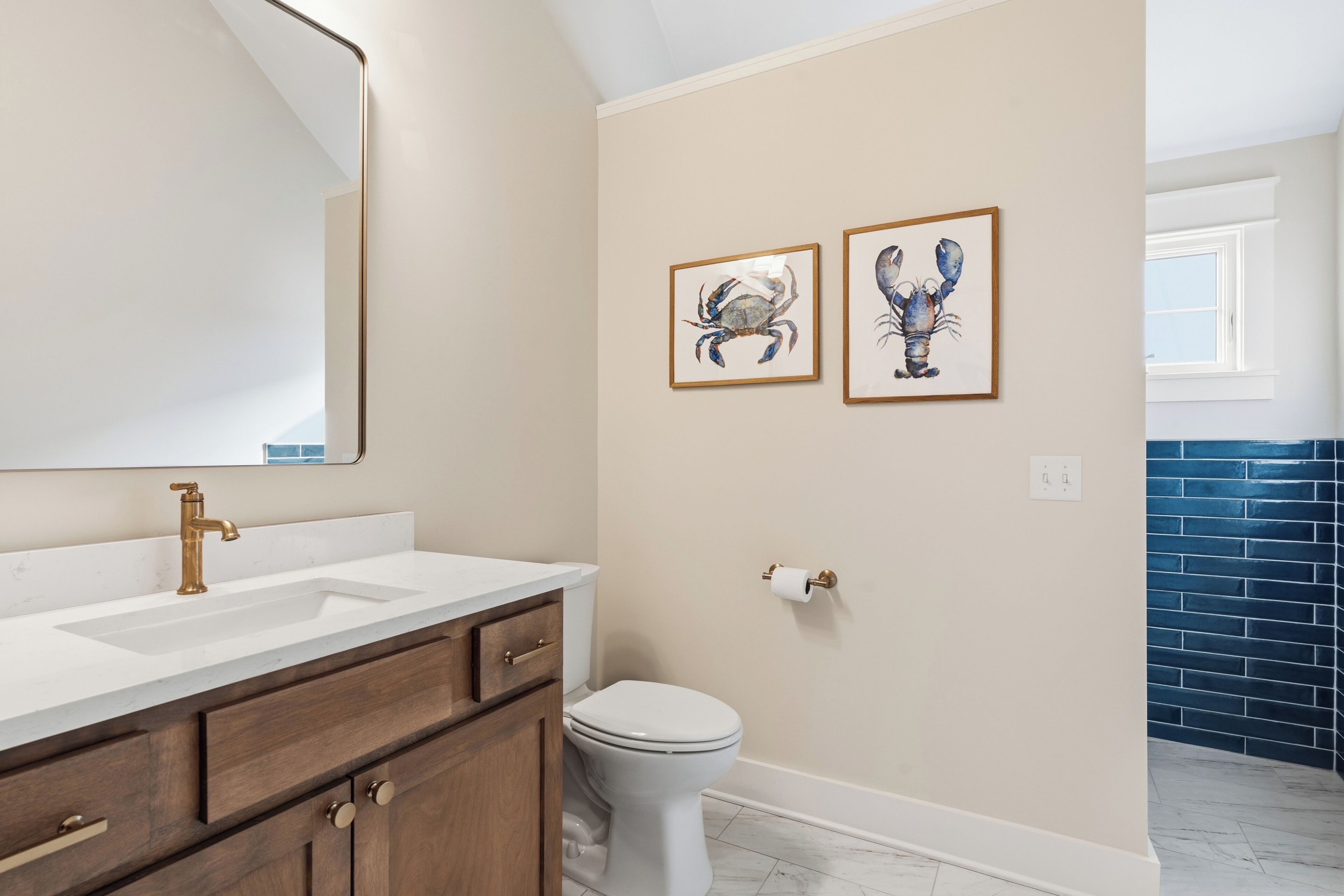Un baño con lavamanos blanco, grifo dorado, tocador de madera, inodoro blanco y dos cuadros enmarcados.