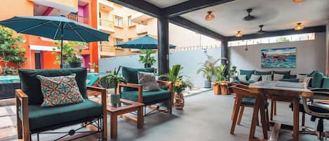 An outdoor seating area with green sofas and tables, surrounded by potted plants and umbrellas.
