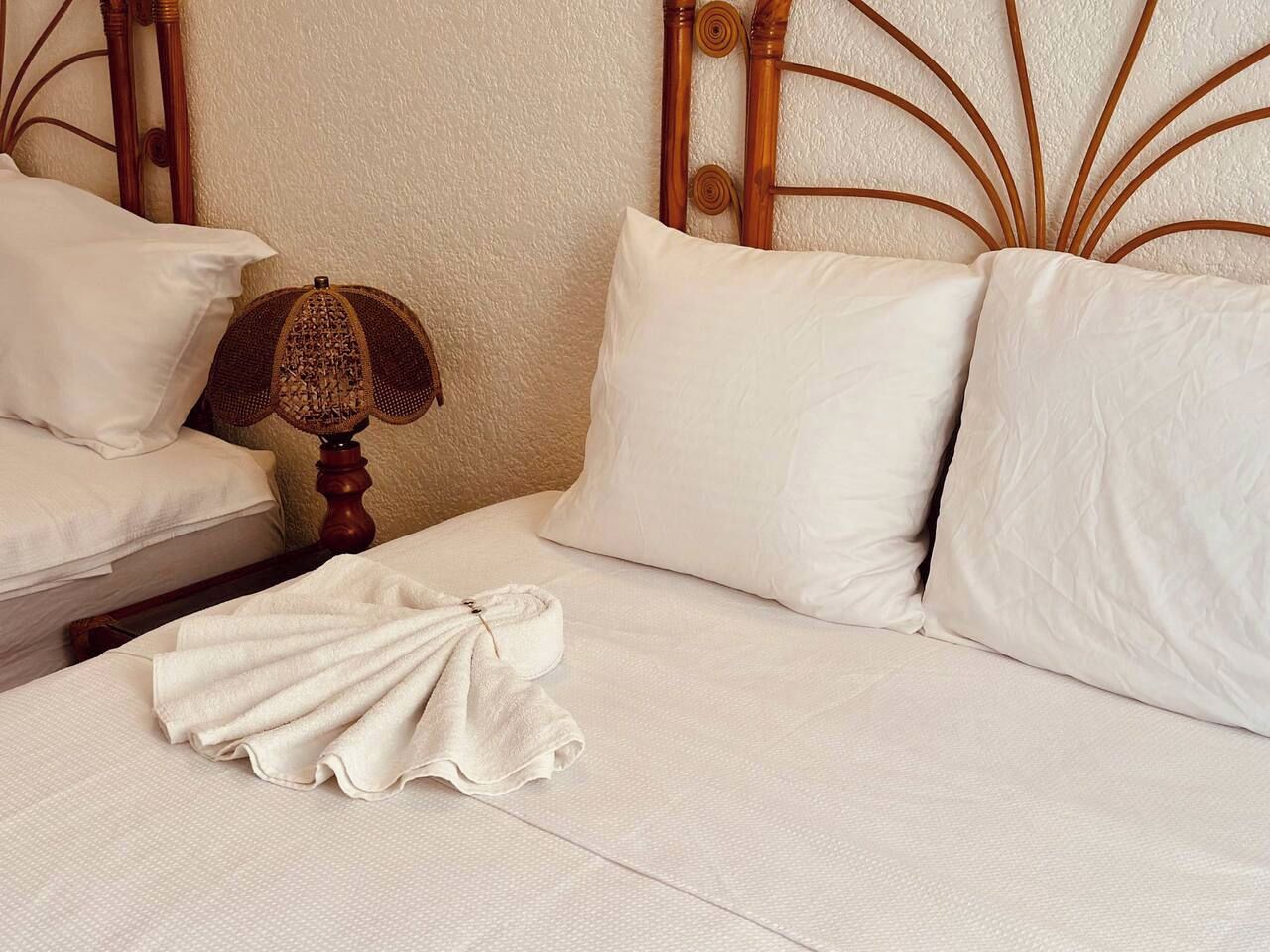 A neatly made bed with white linens, a wooden headboard, and a single white pillow.
