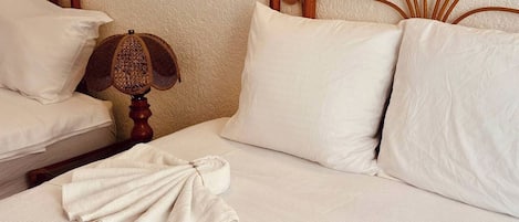 A neatly made bed with white linens, a wooden headboard, and a single white pillow.