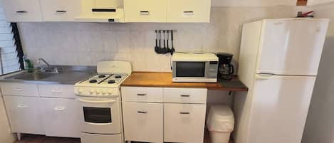 A compact kitchen with white cabinets, a stove, a microwave, and a refrigerator.