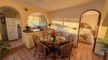 Uma sala de jantar com mesa redonda, cadeiras e cozinha ao fundo.