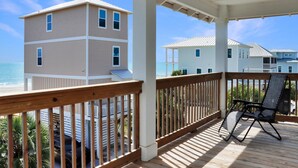 A wooden deck with a chair, overlooking a beach and buildings. - Sand Casas (Port St. Joe)