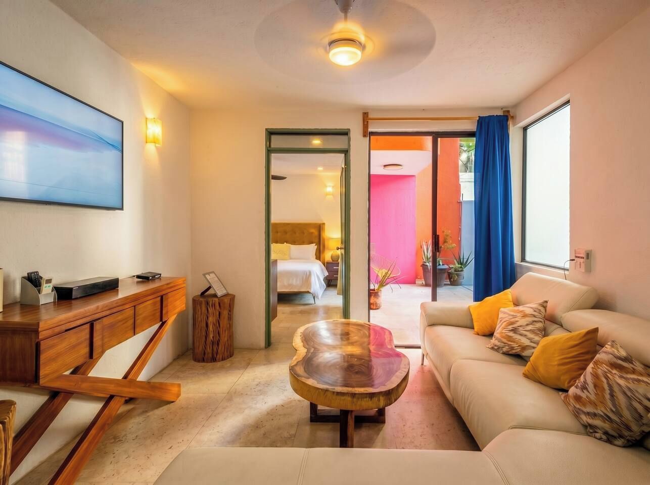 Un salon moderne avec un bureau en bois, une table basse ronde, un canapé avec des coussins et un lit à l’arrière-plan.