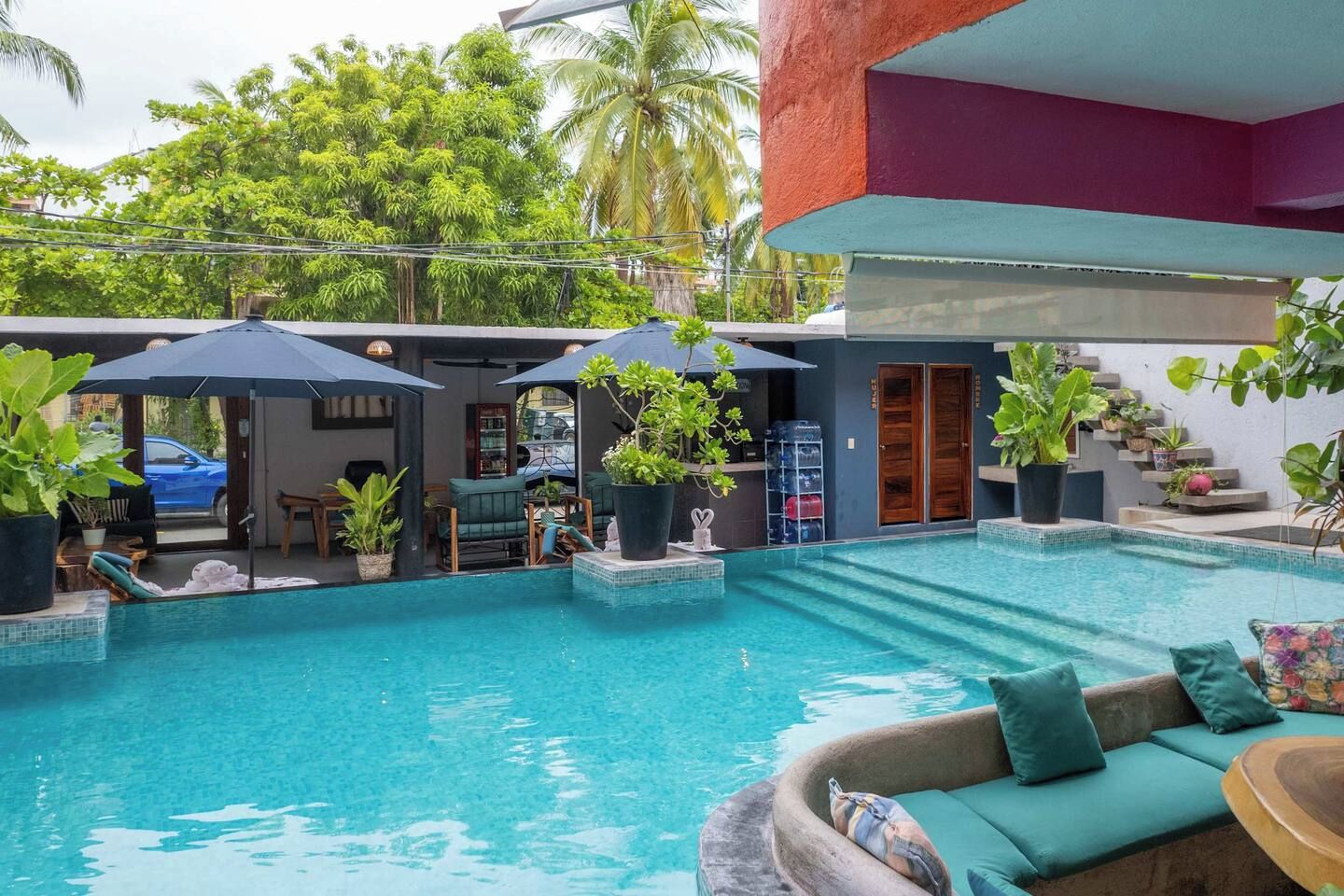 Una piscina con zona de descanso, mobiliario exterior y plantas en macetas.