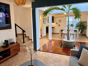 A modern living room with a staircase, a large potted plant, and a dining area with white chairs. - Minimalism Apartment at Ixtapa Zihuatanejo (Ixtapa Zihuatanejo)