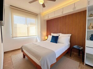 Ein Hotelzimmer mit Bett, Nachttisch, einer Ablage mit Dekoration und einem Fenster mit Jalousien.