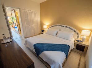 Een verzorgde hotelkamer met een bed, nachtkastjes, een bureau en een deur naar een buitenruimte.
