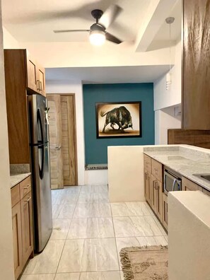 A kitchen with a refrigerator, cabinets, a ceiling fan, and a bull painting on the wall. - Private Condo with Short Walk to La Ropa Beach (Zihuatanejo)