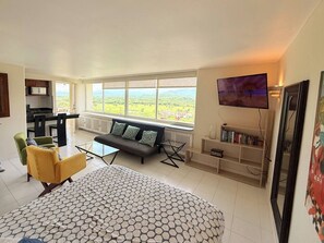 A spacious living room with a sofa, a yellow armchair, a coffee table, and a large window offering a view of greenery. - Elegant Beachfront Studio in Monarca Ixtapa (Ixtapa)