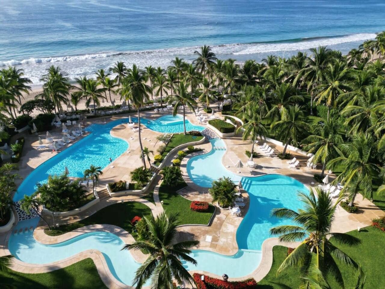 A resort with multiple swimming pools, palm trees, and a beach view.