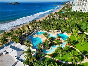 A resort with multiple swimming pools, a beach, and palm trees. - Elegant Beachfront Studio in Monarca Ixtapa (Ixtapa)
