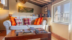 A cozy living room with a sofa, a coffee table with books, a bookshelf, and a window with a view. - The Nest, Hamlet in Tuscany – Mountain View, Private Terrace & Wi-Fi (Ravi)