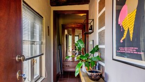 A hallway with a wooden door, a window with blinds, a potted plant, a framed poster, and a staircase leading to another room. - The Nest, Hamlet in Tuscany – Mountain View, Private Terrace & Wi-Fi (Ravi)