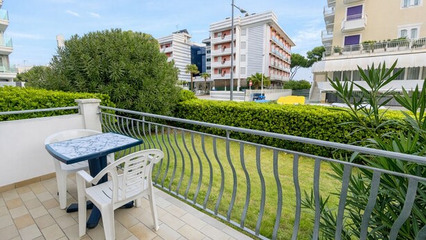 Un balcon avec une table et des chaises, une haie et une vue sur des immeubles à plusieurs étages.
