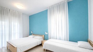Une chambre d’hôtel avec deux lits, un mur d’accent bleu, des rideaux blancs et un sol carrelé.
