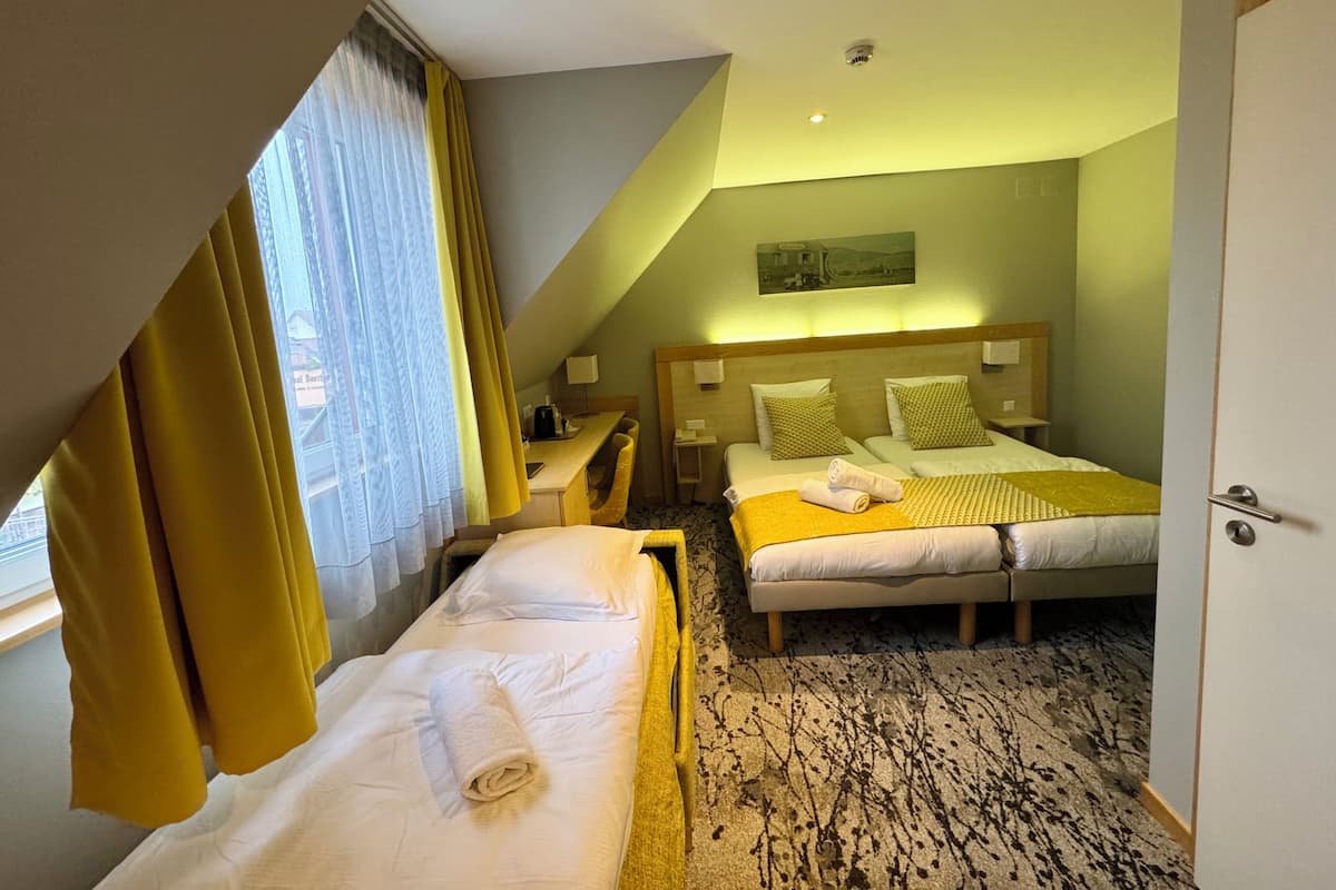 Ein Hotelzimmer mit zwei Betten, einem Schreibtisch, einem Stuhl und einem Fenster mit Vorhängen.