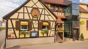 A traditional half-timbered building with a restaurant sign, a visible staircase, and a modern glass extension. - Logis Hôtel Restaurant & Spa Au Soleil (Wettolsheim)
