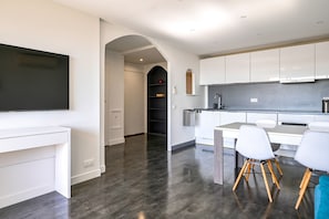 Een moderne keuken met witte kasten, een flatscreen televisie en een eethoek met witte stoelen.
