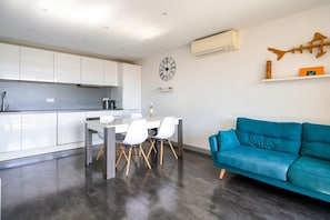 Een moderne keuken met witte kasten, een eettafel met stoelen, een blauwe bank en een wandklok.