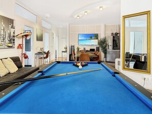 Ein Zimmer mit Billardtisch, einer Sitzecke, einem Essbereich und einem Fernseher.