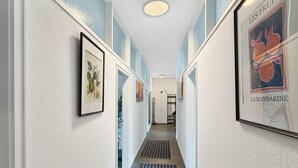 A hallway with framed artwork on the walls, a vent on the floor, and a door at the end.