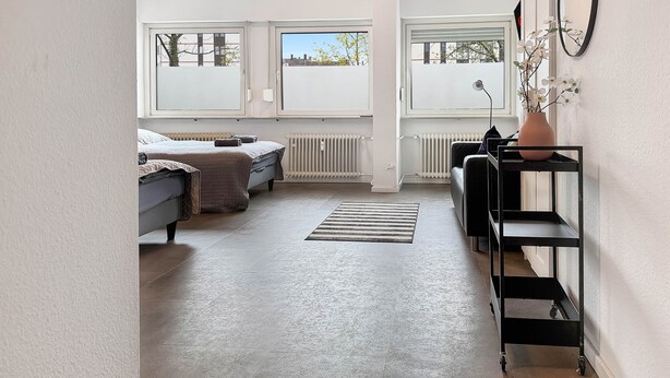 A modern room with a bed, a radiator, a window, a shelf, and a potted plant.