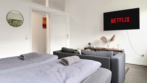 A modern hotel room with a bed, two sofas, a TV mounted on the wall, and a door leading to another room.